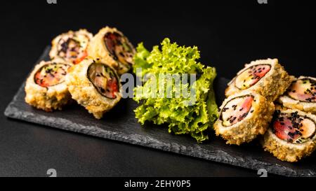 Benutzerdefinierte Sushi-Rolle in Tempura mit Nori, frischem Lachs, Thunfisch, Avocado, Masago-Kaviar, beträufelt mit Ananassauce mit Salat gießen als Dekoration auf Stockfoto