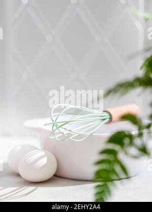 Eierbesen, mit einem Holzgriff, Eiern und einer weißen Schüssel auf weißem Hintergrund reinigen. Selektiver Fokus Stockfoto