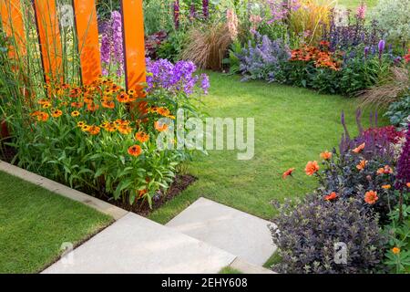 Ein kleiner englischer Garten - Steintreppe führt zu einem Rasengras mit Blumenbeeten gefüllt mit Blumen Pflanzen einschließlich Helenium - Dahlien England GB UK Stockfoto