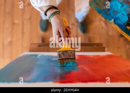 Blue and red abstract paintings. Woman holding paintbrush and working at her canvas on easel. Directly above Stockfoto