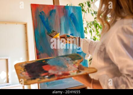 Künstlerin zeichnet Acrylmalerei auf Staffelei in ihrem Atelier. Frau hält Palette und schafft Acryl abstrakte Gemälde im Studio Stockfoto