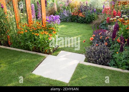 Ein kleiner Garten - Steintreppe führt zu einem Rasengras Bereich mit Blumenbeeten gefüllt mit Blumen Pflanzen einschließlich Helenium - Dahlien England GB Großbritannien Stockfoto