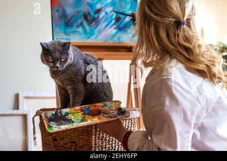 Frau und ihr Haustier im Kunststudio. Künstlerin, die gerne mit ihrer britischen Kurzhaarkatze malt. Handwerk und Freizeitaktivitäten im Innenbereich Stockfoto