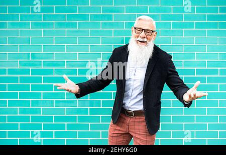 Fröhlicher Hipster Mann auf Willkommens-Stimmung posiert gegen türkisfarbene Wand Hintergrund - trendige alte Person tragen lässige Mode Kleidung - Glückliches älteres Leben Stockfoto