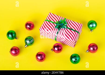 Weihnachtskarte mit Geschenkbox und glänzenden Kugeln auf gelbem Hintergrund. Bunte Neujahr Hintergrund, festliche Dekorationen Stockfoto