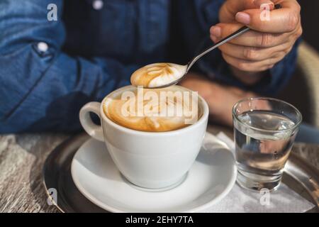 Cappuccino, Frau trinkt Kaffee im Café. Nahaufnahme des Löffels in der weiblichen Hand und der weißen Kaffeetasse Stockfoto