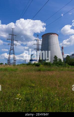 Wärmekraftwerk mit Hochspannungsleitungen im Hintergrund Einer Sommerwiese vertikale Ausrichtung Stockfoto