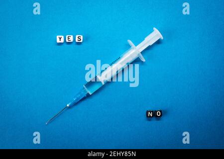 Ja Nein Wörter aus quadratischen Buchstaben und einer Spritze auf blauem Hintergrund. Vor- und Nachteile des Coronavirus-Impfstoffs, Bedenken und Zweifel an der Impfung Stockfoto