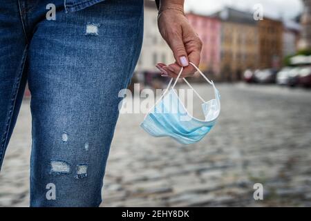 Frau hält Gesichtsmaske in der Hand auf der Stadtstraße während COVID-19 Epidemie Krise. Das Ende des Coronavirus-Pandemiesperrkonzepts Stockfoto