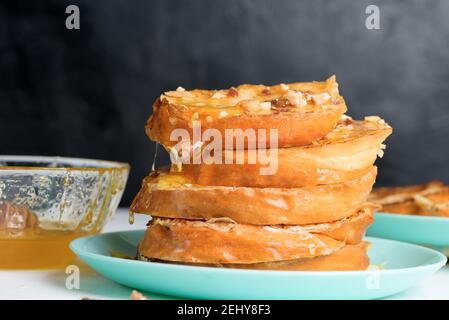 Hausgemachter French Toast gebraten mit Honig und Nüssen auf einem blauen Teller auf einem dunklen Hintergrund. Eingeweicht in Milch-Ei-Mischung. Gesundes Frühstück. Nahaufnahme. Stockfoto