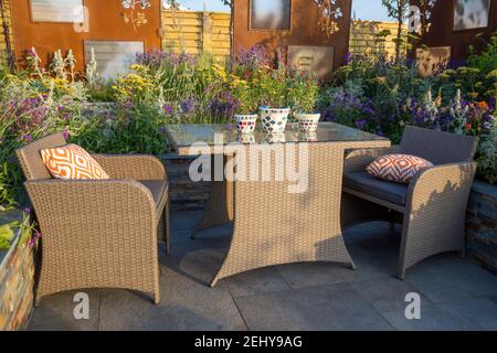 Terrasse im modernen Gartendesign mit Acrylrattan-Essmöbeln mit Gartenmöbeln, Tisch und Stühlen, orangefarbenen Kissen, erhöhten Betten UK Stockfoto