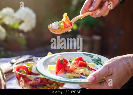 Frau serviert Gemüsesalat mit Holzlöffel auf dem Teller. Genießen Sie gesunde vegetarische Speisen im Freien. Stockfoto