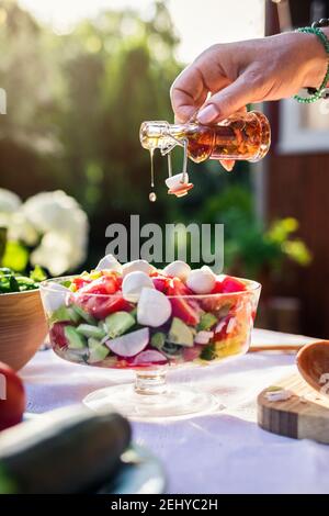 Frau Hand Gießen aromatisierten Olivenöl zu frischem Gemüsesalat. Vorbereitung gesunde vegetarische Nahrung für Gartenparty im Freien Stockfoto