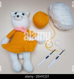 Handgemachtes Strickspielzeug. Spielzeug weiße Maus in einem orangen Rock mit Stricknadeln auf einem grauen Hintergrund. Gehäkelte Stofftiere. Stockfoto