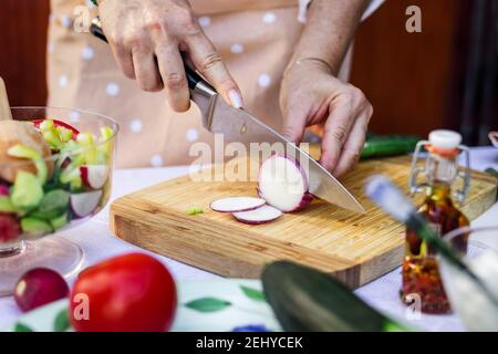 Frau schneidet rote Zwiebel mit Küchenmesser auf Holzbrett. Zubereitung von Speisen. Nahaufnahme weibliche Hand Chooping Gemüse Stockfoto
