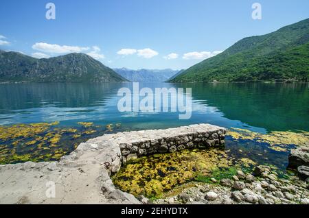 Blick auf die Bucht von Kotor mit Reflexionen der Berge und Steinpier, Blick auf Perast und Kostanijca, Montenegro von Flavia Brilli Stockfoto