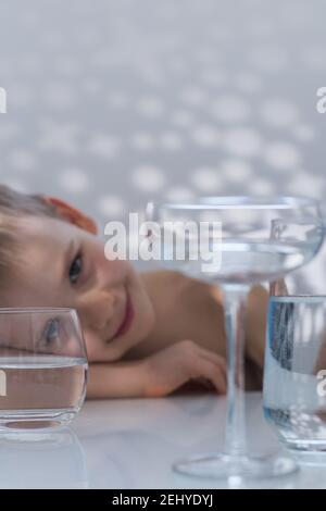 Porträt eines Jungen durch Gläser Wasser. Verzerrtes Glas Wasser. Kunstkonzept eines gesunden Lebensstils. Stockfoto