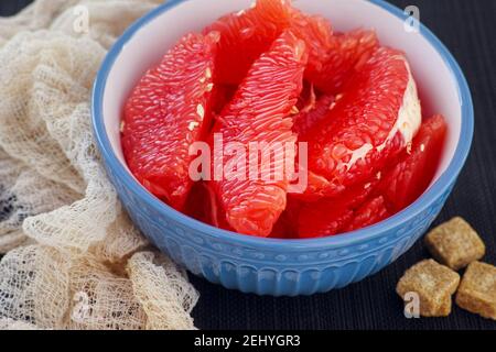 Scheiben frische Bio-Grapefruit in einer Schüssel und einige braune Rohrzucker-Würfel in der Nähe. Nahaufnahme. Stockfoto