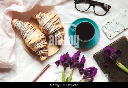 Frühstück im Bett. Morgen, Croissant, Kaffee, Blumen und ein Notizbuch mit einem Stift. Planung Stockfoto