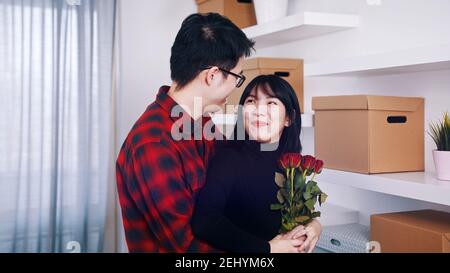 Alles Gute zum Jahrestag. Ehemann umarmte seine Frau in der neuen Wohnung. Frau mit roten Rosen. Hochwertige Fotos Stockfoto