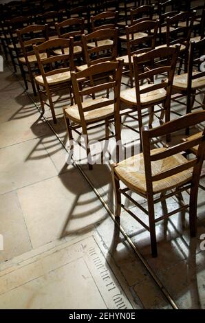 Reihen leerer Holzstühle werfen Schatten in einem schwach beleuchteten Raum in einer Kirche in Frankreich Stockfoto