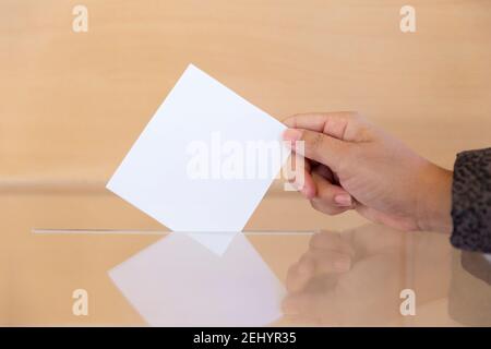 Nahaufnahme der Hand einer Person Einlegen eines leeren Umschlags in eine Wahlurne. Leerzeichen für Text. Stockfoto