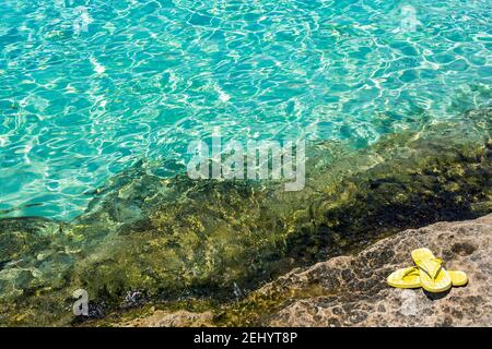 Blick auf das türkisfarbene Wasser in der Blauen Lagune mit gelben Flip Flops, Comino Island, Malta Stockfoto