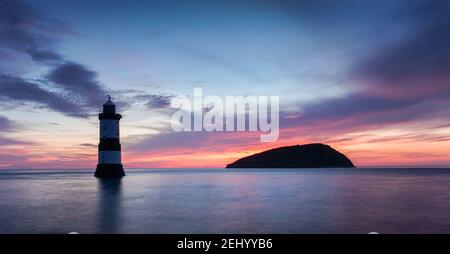 Sunrise in Penmon Point, Anglesey, Wales, Vereinigtes Königreich. Penmon (Trwyn Du) Leuchtturm und Puffin Island. Dramatische, bunte skiy und glatte Meer. Stockfoto