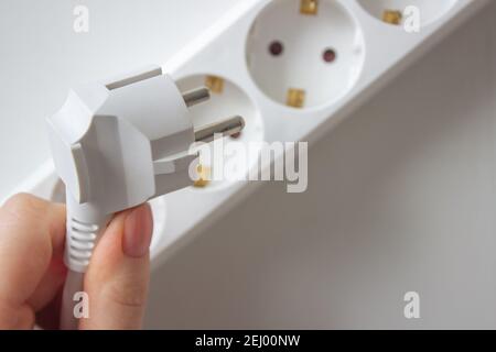 Hand hält weißen Stecker aus weißer Steckdose auf weißem Hintergrund Stockfoto