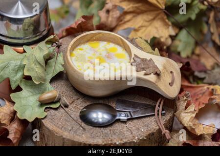Skandinavische Küche, Fischsuppe mit Sahne, in einem Holzkrug, Thermoskanne und einem Löffel, auf einem Stumpf umgeben von trockenen Blättern. Hochwertige Fotos Stockfoto