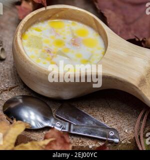 Skandinavische Küche, Fischsuppe mit Sahne, in einem Holzkrug, Thermoskanne und einem Löffel, auf einem Stumpf umgeben von trockenen Blättern. Hochwertige Fotos Stockfoto