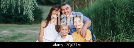 Happy Caucasian Familie von vier Personen im Park im Freien am Sommertag. Mutter und Vater umarmen zwei Söhne Brüder Geschwister. Lifestyle authentisch natura Stockfoto