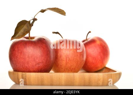 Drei ganze rote reife Bio-Äpfel liegen auf einem Bambustablett auf weißem Grund. Stockfoto