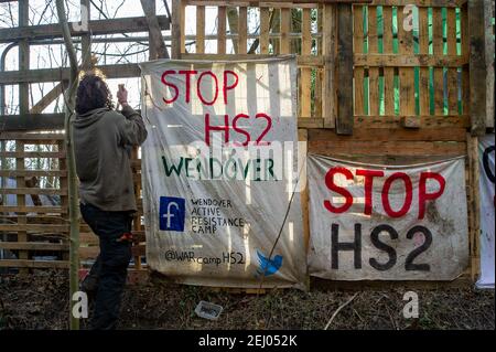 Aylesbury, Buckinghamshire, Großbritannien. 20th. Februar 2021. Ein Protestler fastet vor dem neuen Protestlager ein Stop HS2 Banner. HS2 Ltd übernahm ein Holz namens Spinney Anfang dieser Woche und haben begonnen, es zu zerstören. Stop HS2 Aktivisten haben ein neues Lager in den Wäldern in der Nähe aufgebaut, um HS2 daran zu hindern, die Bäume zu Fällen. Die Zahl der Demonstranten wächst von Tag zu Tag, da die Menschen sehen, wie zerstörerisch die Hochgeschwindigkeitsbahn von London nach Birmingham für die Umwelt ist. Quelle: Maureen McLean/Alamy Live News Stockfoto