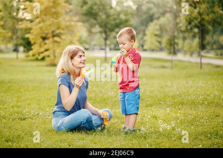 Junge kaukasische Mutter und Junge Kleinkind Sohn Blasen Seifenblasen im Park. Mutter und Kind spielen Spaß zusammen im Freien am Sommertag. Glücklich Stockfoto