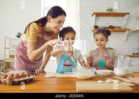 Liebevolle Mutter in der Küche lehrt ihre kleinen Zwillingstöchter, einen Kuchen oder Kekse zu machen. Stockfoto