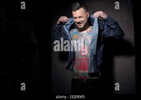 Junger schöner Männlicher Mann, in unbefestigtem Jeanshemd mit Tätowierung auf der Brust. Stockfoto