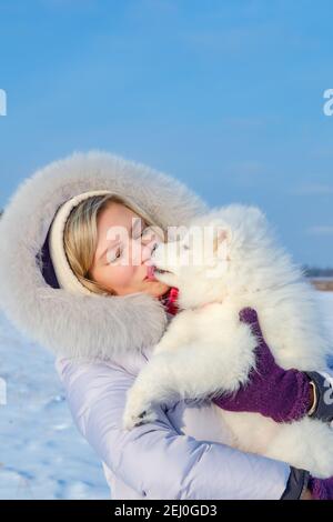 Lachende junge Frau und samoyed Welpen Kuss auf Winter frostig Tag Stockfoto