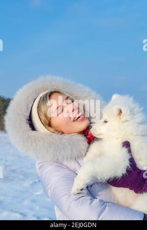 Lachende junge Frau und samoyed Welpen Kuss auf Winter frostig Tag Stockfoto