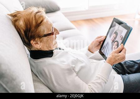 Hohe Winkelansicht der zufriedenen älteren Frau, die auf ruht Sofa zu Hause und mit Videoanruf mit der Familie während Mit Tablet Stockfoto