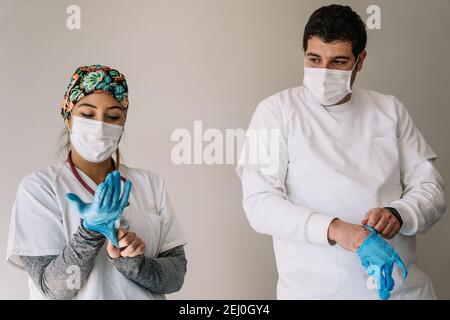 Männliche und weibliche Ärzte in medizinischen Masken stehen im Krankenhaus Und das Anziehen von Latexschutzhandschuhen während der Arbeit während des Coronavirus Pandemie Stockfoto