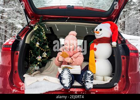 Im kofferraum des autos gibt es einen schneebedeckten weihnachtsbaum und  mandarinen auf einer blauen decke, das auto steht im winterwald