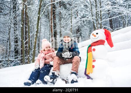 Niedlichen Jungen und Mädchen Gebäude Schneemann im Winterwald Stockfoto