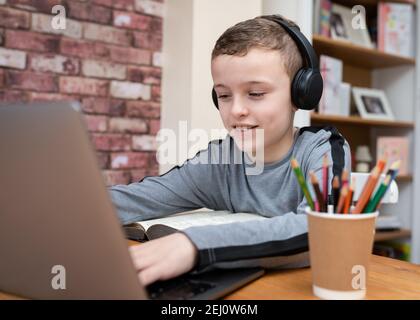 Kleiner Junge glücklich lächelnd arbeitet hart zu Hause mit Laptop Computer und kabellose bluetooth-Kopfhörer für Hausaufgaben und Schularbeiten Remote Stockfoto