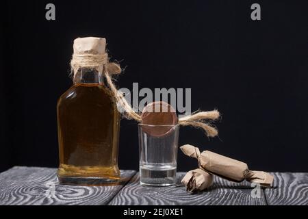Geschenk Alkohol. Eine Flasche Alkohol ist auf den Brettern. In der Nähe ist ein Glas und Süßigkeiten. Nahaufnahme. Stockfoto