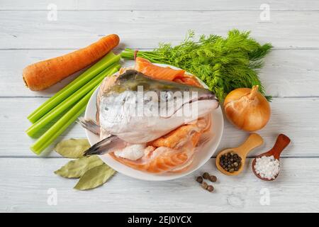 Rohzutaten zum Kochen von Fischfond: Frischer Lachskopf und -Knochen, Gemüse, Salz und Pfeffer auf dem weißen Holztisch. Rote Fischbrühe Bouillon Rezept Stockfoto