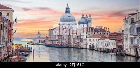 Atemberaubende Aussicht auf die Skyline von Venedig mit dem Canal Grande und der Basilika Santa Maria della Salute in der Ferne bei einem dramatischen Sonnenaufgang. Stockfoto