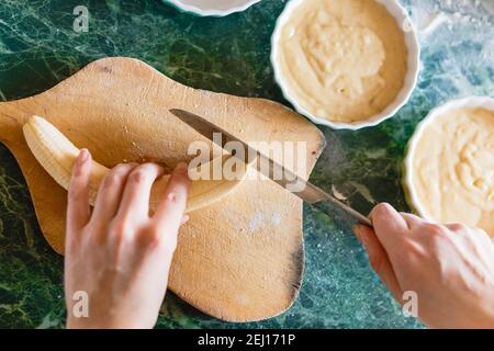 Frau schneidet eine Banane mit einem Messer auf unhöflichem Holzbrett. Draufsicht Stockfoto