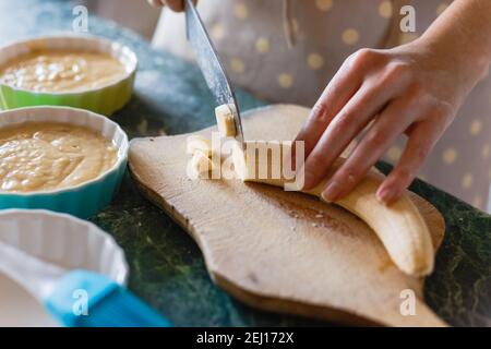 Frau schneidet eine Banane mit einem Messer auf unhöflichem Holz Platine Stockfoto
