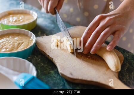 Frau schneidet eine Banane mit einem Messer auf unhöflichem Holzbrett. Stockfoto